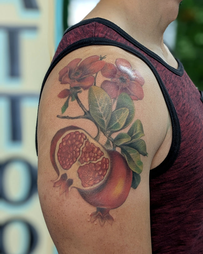 hyperrealistic pomegranate fruit tattoo – full color shoulder piece with branch and flower