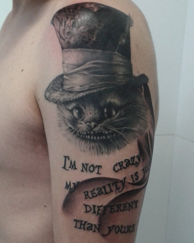 hyperrealistic Cheshire Cat tattoo from Alice in Wonderland – black and grey half sleeve with text ‘I’m not crazy, my reality is just different than yours’