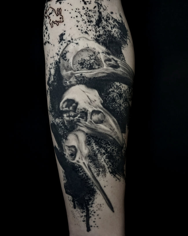 realistic raven skull tattoo – black and grey forearm piece with heavy black ink splash pattern