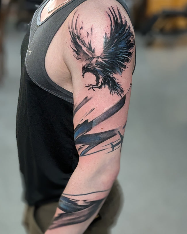 graphic black and blue sleeve tattoo – illustrative raven with heavy black brushstrokes, trash polka inspired
