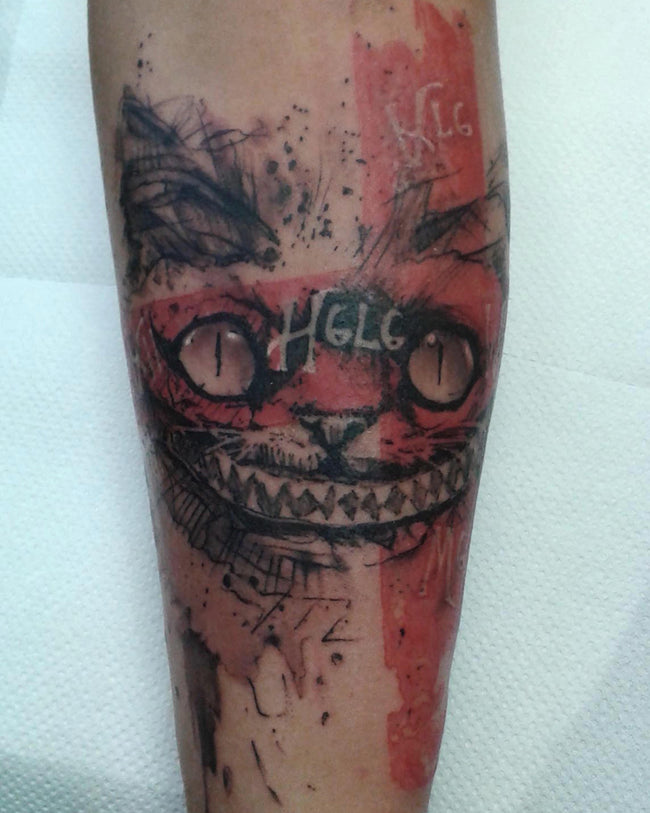 graphic illustrative Cheshire Cat tattoo – black and red forearm piece inspired by trash polka style